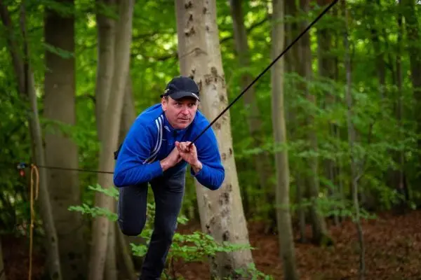 Mann nutzt Seilbrücke zwischen Bäumen zur Fortbewegung im Wald