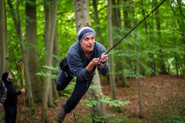 Mann schwingt an einem Seil zwischen Bäumen im Wald