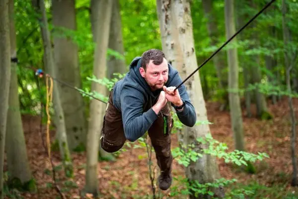 Mann schwingt an einem Seil zwischen Bäumen im Wald