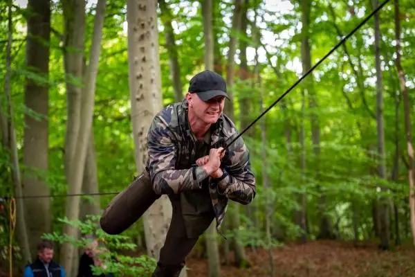 Mann schwingt an einer Seilbrücke zwischen Bäumen im Wald