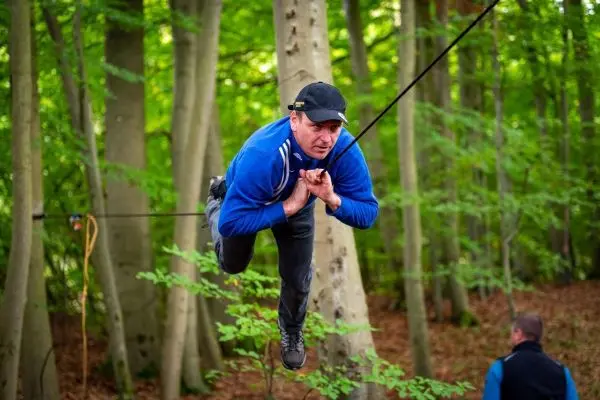 Mann schwingt an einer selbstgebauten Seilbrücke zwischen Bäumen