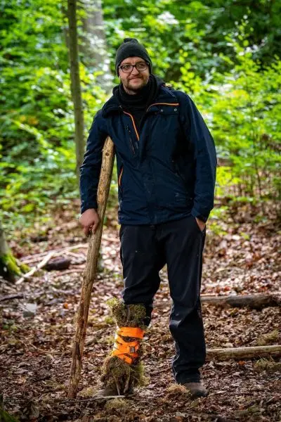 Mann steht im Wald neben einem Stock und trägt eine improvisierte Beinbandage