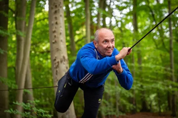 Mann zieht sich an einem Seil in einem Wald hoch
