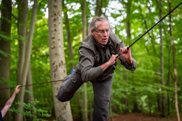 Person balanciert auf einem gespannten Seil zwischen Bäumen