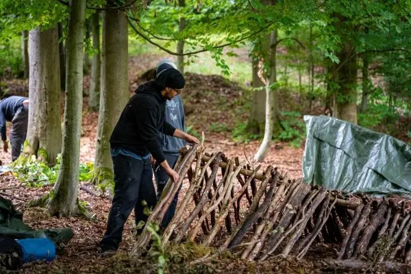 Person baut eine Struktur aus Ästen im Wald beim Survival Training