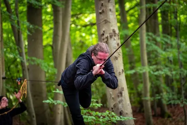 Person nutzt Seil für eine selbstgebaute Seilbrücke zwischen Bäumen