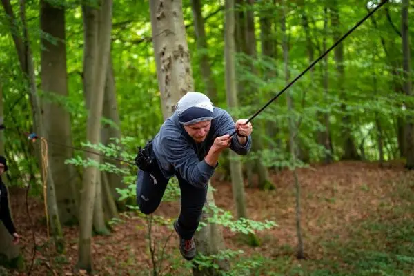 Person schwingt an einem Seil zwischen Bäumen im Wald