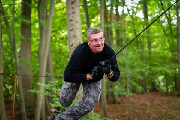 Person schwingt an einer Seilbrücke zwischen Bäumen im Wald