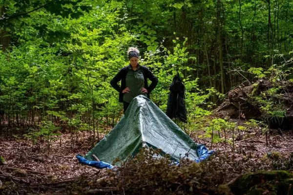 Tarp-Notunterkunft wird im Wald aufgestellt und gesichert