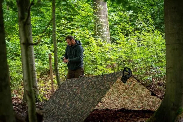 Tarp-Notunterkunft wird im Wald mit Schnüren befestigt