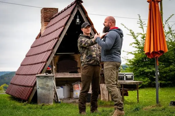 Zwei Männer üben eine Technik vor einer Holzkonstruktion mit rotem Dach