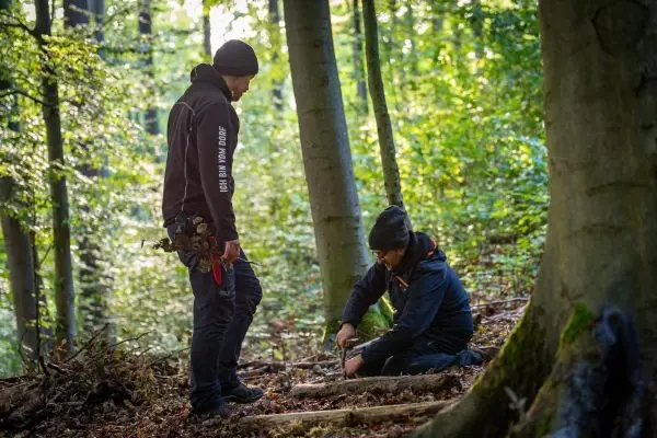 Zwei Personen arbeiten im Wald an einer Holzstruktur auf dem Boden