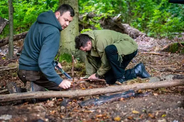 Zwei Personen bearbeiten Holzstücke am Boden im Wald