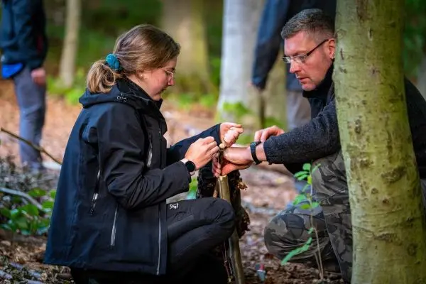 Zwei Personen binden eine Schnur um einen Stock im Wald