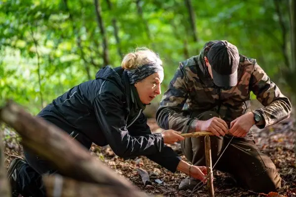 Zwei Personen konstruieren eine Feuerbohrvorrichtung aus Holz im Wald