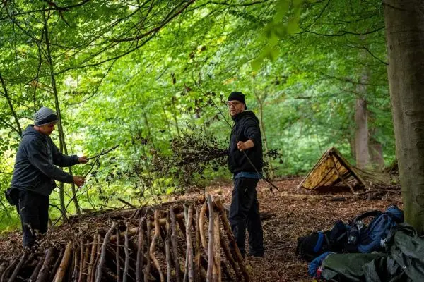 Zwei Personen sammeln Äste und Zweige für eine Notunterkunft im Wald