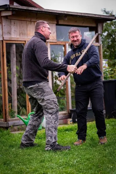 Zwei Personen üben den Umgang mit einem Stock in einem Garten