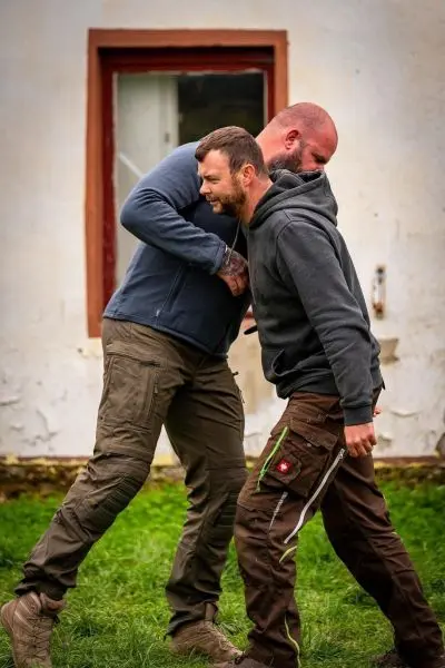 Zwei Personen üben eine Nahkampftechnik in einem Trainingsszenario