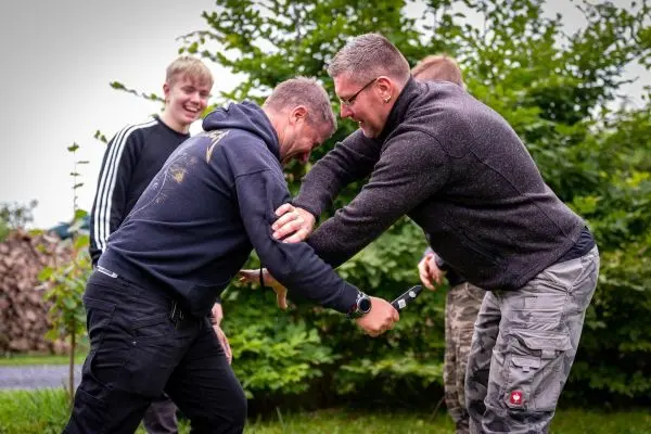 Zwei Personen üben einen Nahkampf mit einem Messer in einer grünen Umgebung