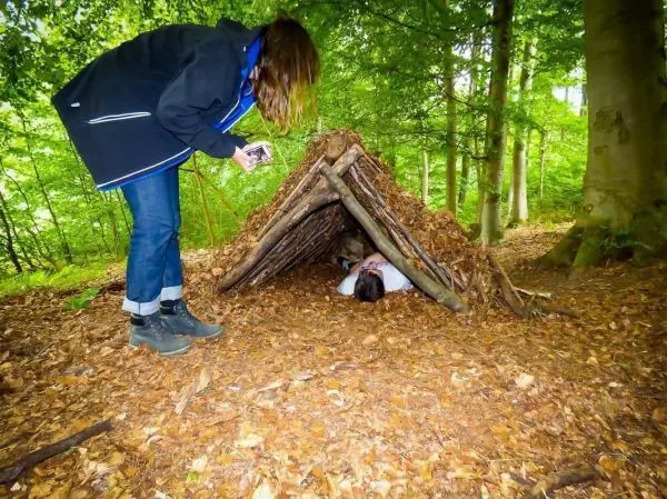 Frau fotografiert eine improvisierte Laubhütte im Wald