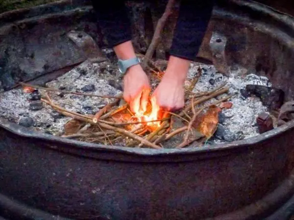 Hände fügen Zunder und Äste in ein Feuer im Feuergrube hinzu