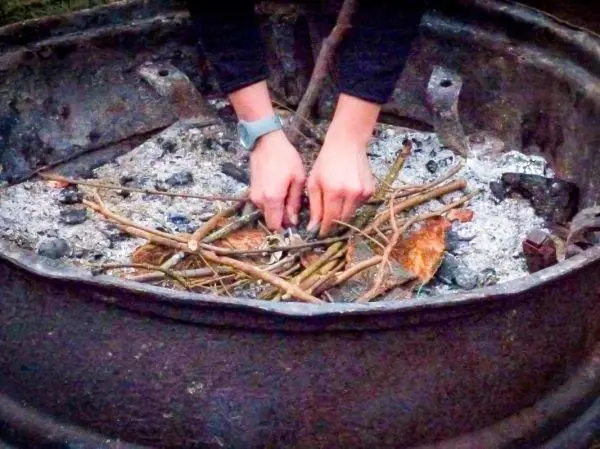 Hände legen Zweige in eine Feuerstelle mit Asche und Kohlen