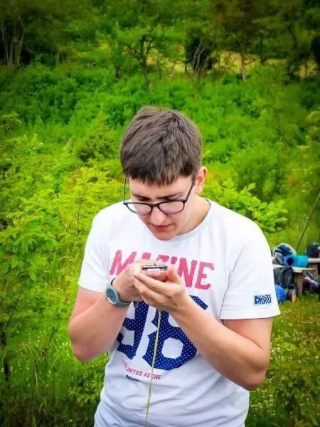 Junger Mann betrachtet Smartphone vor grüner Landschaft