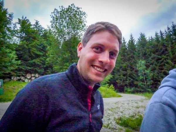 Lächelnder Mann steht vor einer Waldlandschaft mit Bäumen im Hintergrund