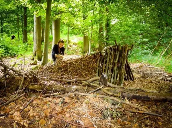 Person baut eine Unterkunft aus Ästen und Blättern im Wald