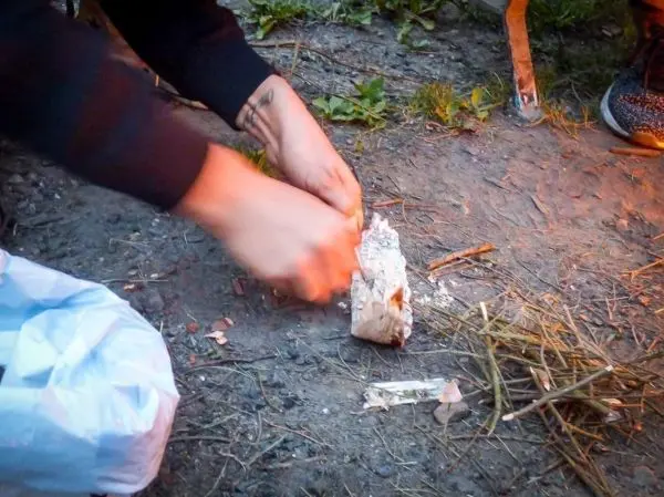 Person zerkleinert Holzstück auf dem Boden beim Überlebenstraining
