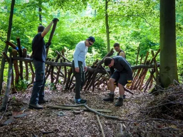 Vier Personen bauen eine Holzstruktur im Wald aus Ästen und Zweigen