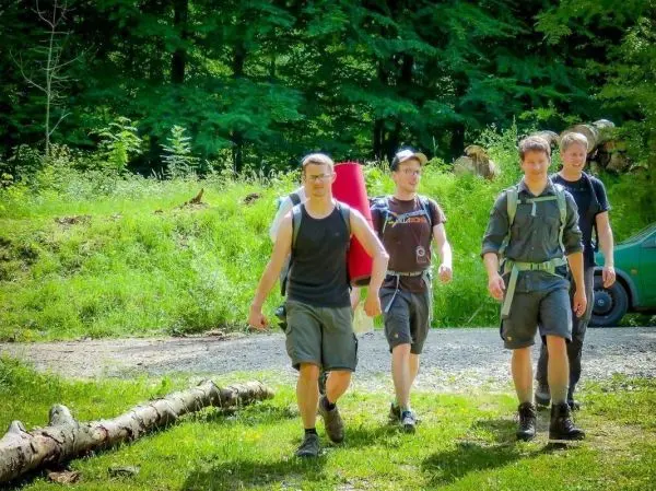 Vier Personen tragen Rucksäcke und gehen auf einem Waldweg