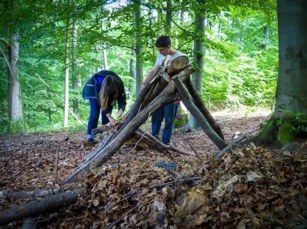 Zwei Personen bauen eine Holzstruktur aus Ästen im Wald