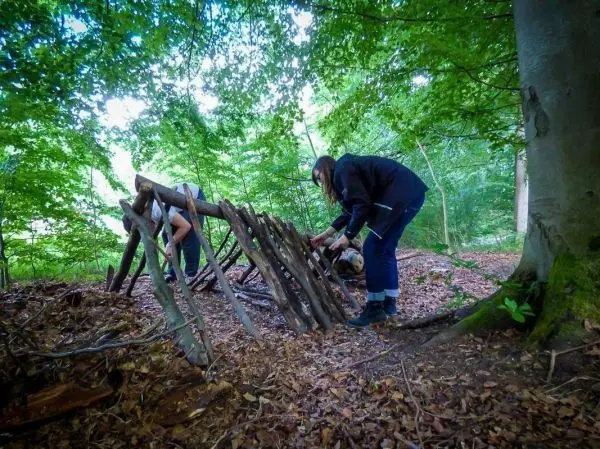 Zwei Personen bauen eine Laubhütte aus Ästen im Wald