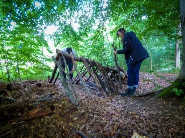 Zwei Personen bauen eine Laubhütte aus Ästen im Wald
