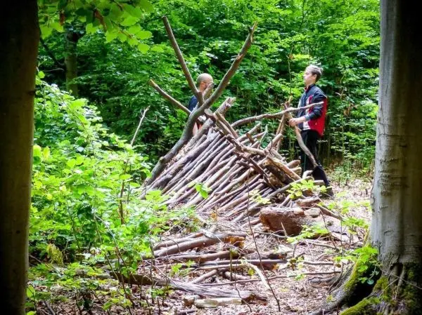 Zwei Personen bauen eine Laubhütte aus Ästen im Wald