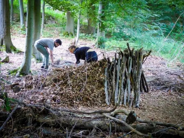 Zwei Personen bauen eine Laubhütte aus Ästen und Blättern im Wald