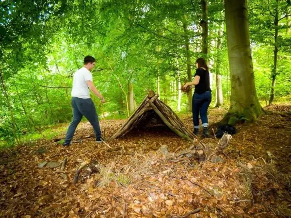 Zwei Personen bauen eine Tarp-Notunterkunft aus Ästen im Wald