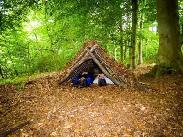 Zwei Personen liegen in einer Tarp-Notunterkunft aus Ästen und Laub