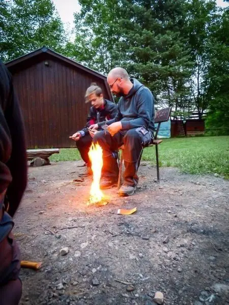 Zwei Personen sitzen am Boden und beobachten ein Feuer