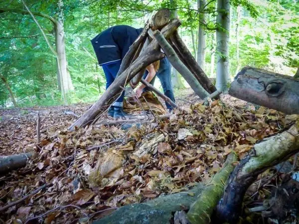 Zweige werden zu einer Tarp-Notunterkunft zusammengefügt und mit Laub bedeckt