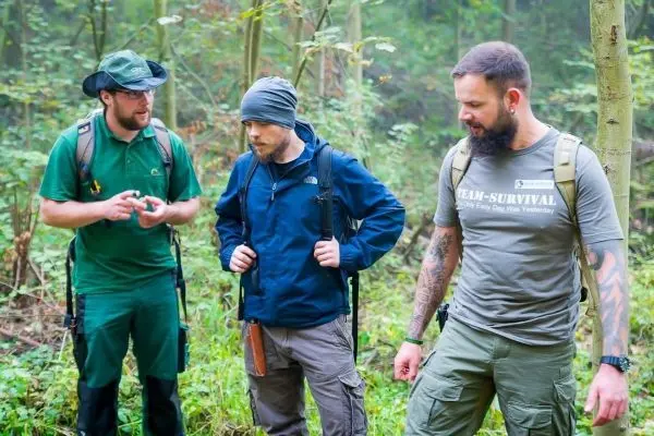 Drei Personen mit Rucksäcken stehen im Wald und diskutieren über Ausrüstung