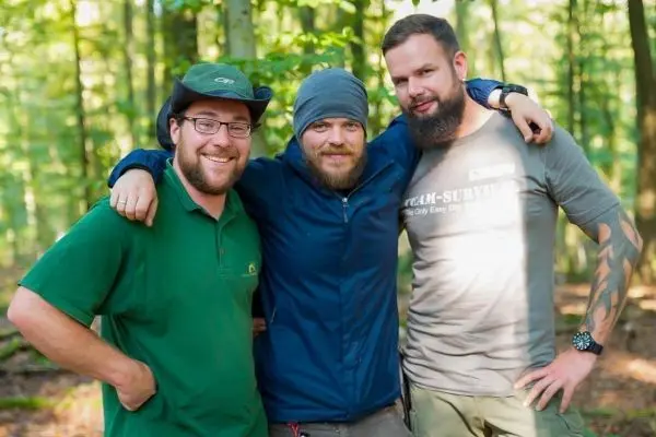 Drei Personen stehen im Wald und lächeln in die Kamera
