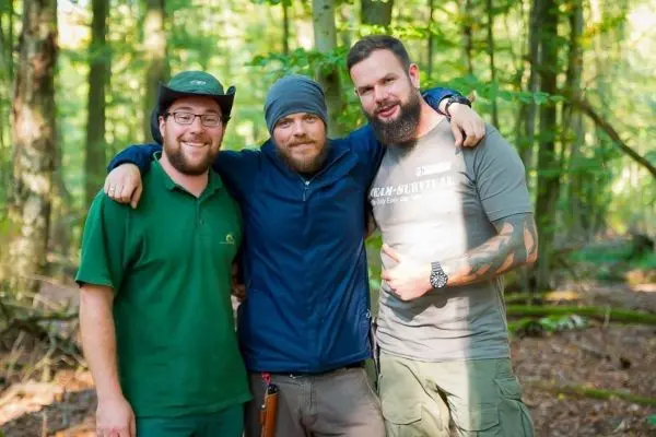 Drei Personen stehen in einem Wald und umarmen sich freundlich