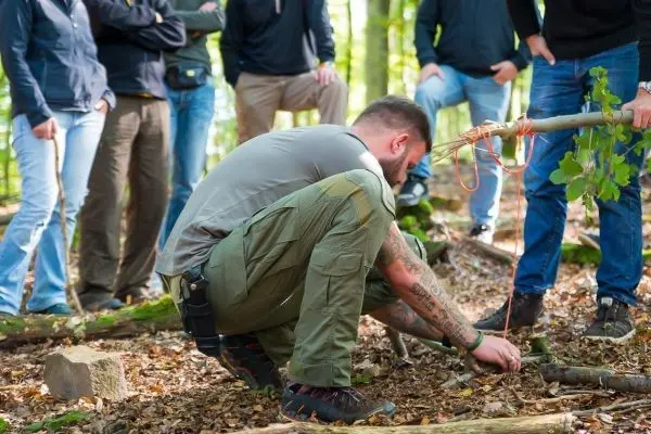 Ein Mann kniet im Wald und richtet eine Schlingenfalle mit einem Stock ein