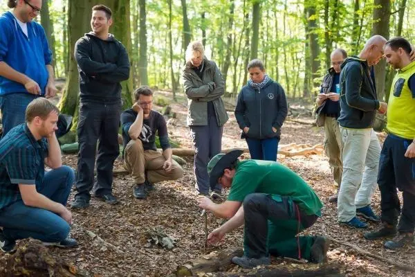 Ein Teilnehmer nutzt einen Feuerbohrer zur Feuererzeugung im Wald