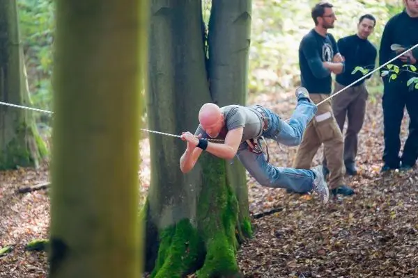 Ein Teilnehmer schwingt an einem Seil zwischen zwei Bäumen im Wald
