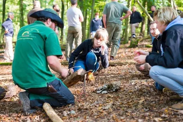 Ein Teilnehmer zündet Zunder mit einem Feuerstahl an einem Holzstück an