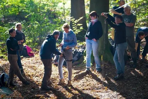 Ein Trainer befestigt eine Sicherungsgurt an einer Teilnehmerin im Wald