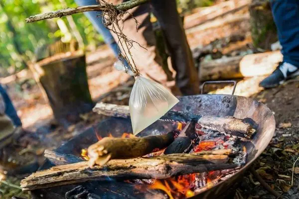 Eine durch einen Stock hängende Tüte über einem Feuer im Wald beim Survival Training